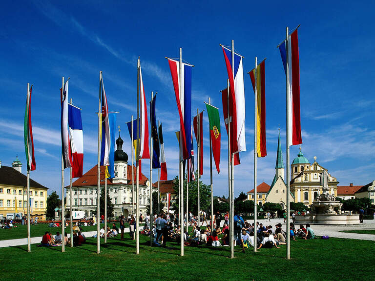 Fahnen verschiedenster Nationen wehen vor dem rege besuchten Kapellplatz in Altöttingen.