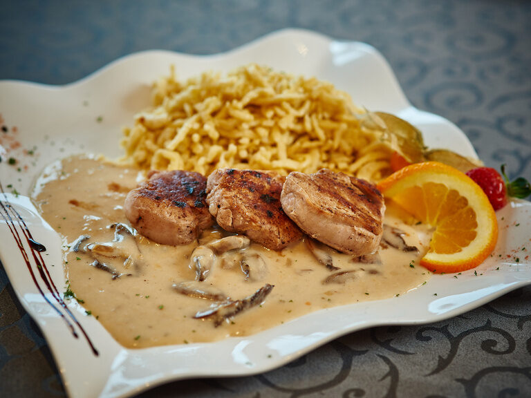 Auf einem Tisch steht ein Teller Spätzle mit einer Sauce und Garnelen