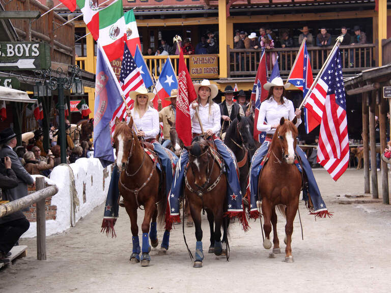 Eine Gruppe von Menschen reitet auf Pferden durch die Straßen von Pullman City Western town im Bayerischen Wald.