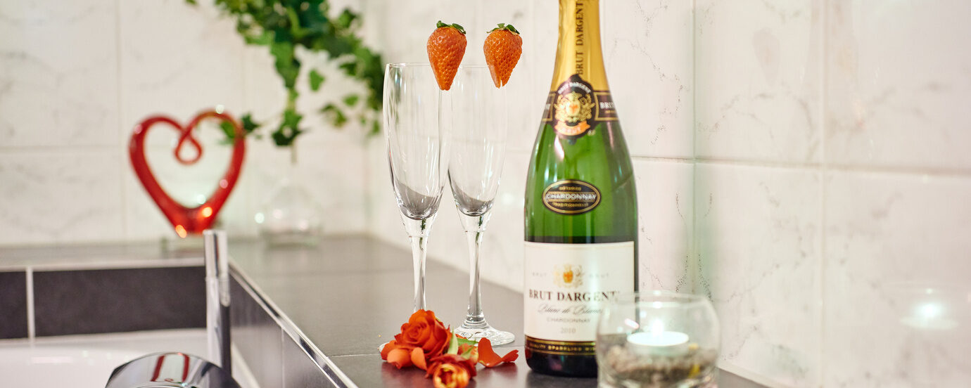 Eine Sektflasche und dazugeh&ouml;rige Gl&auml;ser stehen am Rand einer Badewanne