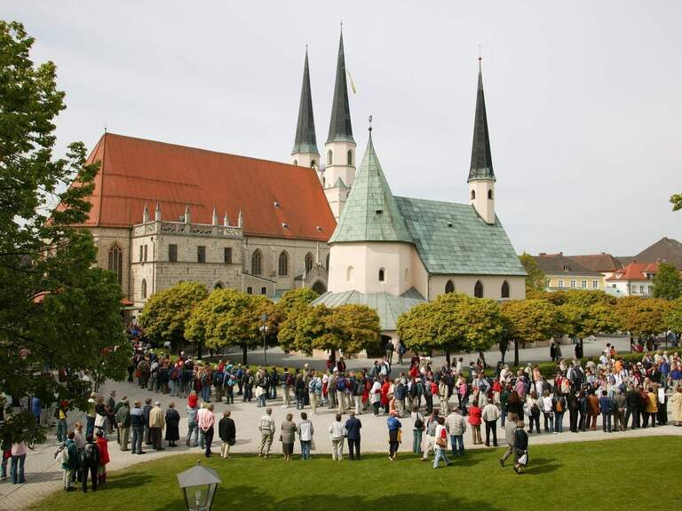 Eine Menschengruppe versammelt sich vor der eindrucksvollen Altöttinger Kirche, einem beliebten Wallfahrtsziel.